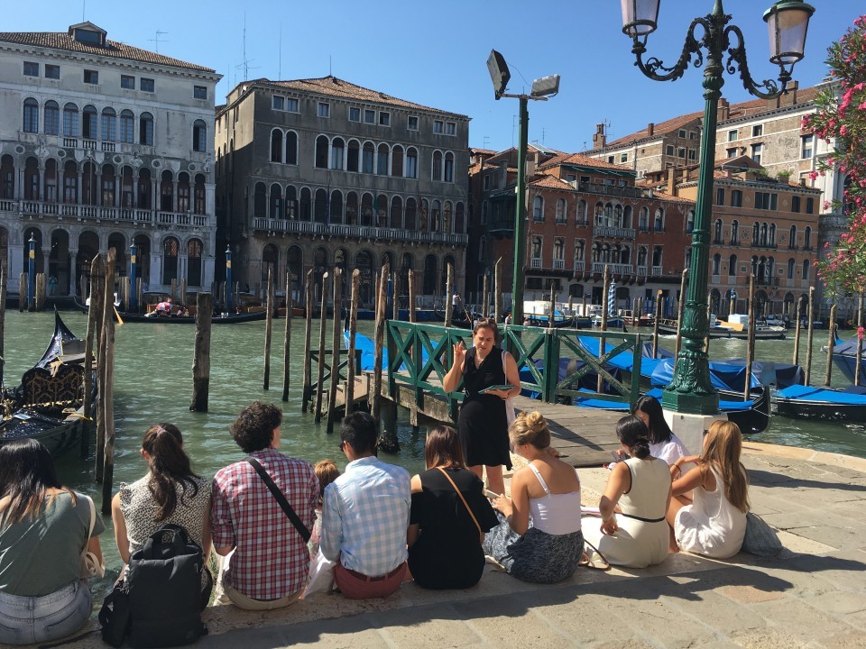 Courses are set up as a field studies, using the city as their classroom with supporting site visits in and outside of Venice. Group of students seated along a Venetian canal receiving instruction